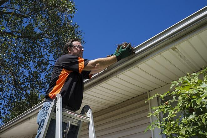 a worker inspecting and repairing a clogged gutter in Ballwin